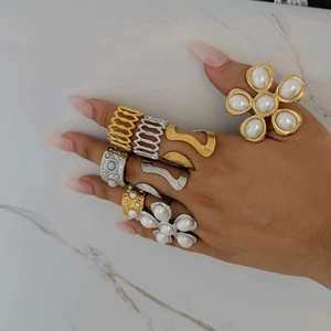Chunky gold and silver flower rings with pearls on hand over white marble background