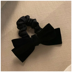 Close-up of a premium black velvet bow hair tie on a soft textured beige fabric