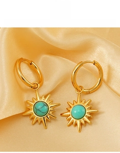Macro view of gold titanium steel sunburst earrings with turquoise stone on silk fabric