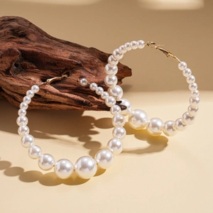 Macro detail of gradient imitation pearls on golden hoop earrings set against dark wood