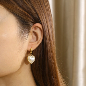 Detailed view of heart-shaped gold earrings with faux pearl and rhinestone inlay