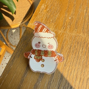 Close-up of a glittery acrylic snowman hair clip on a natural wooden tabletop