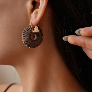 Close-up of deep brown woven leather hoop earring with elegant gold metal accents
