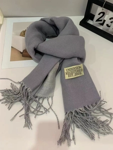 Detail of grey knitted scarf featuring soft tassels and a minimalist brand label