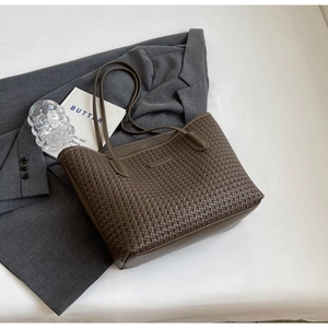 Top view of deep brown woven tote bag on grey blazer with minimalist props