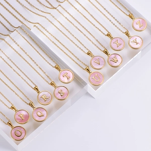 Detailed view of round gold initial necklaces with pink shell pendants on display