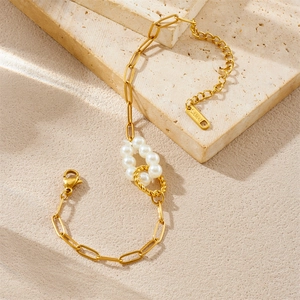 Detail of gold paperclip chain bracelet with pearl accents on a natural stone background