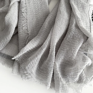 Close-up of light grey cotton linen scarf showing texture and frayed tassel edges