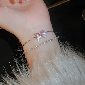 Detail of gold bow bracelet and rectangular zircon tennis chain worn on wrist