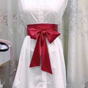 Détail de la large ceinture en satin rouge foncé avec grand nœud sur robe blanche