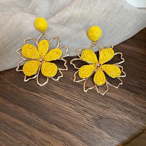 Bohemian yellow raffia flower earrings with gold metal frames on dark wood surface