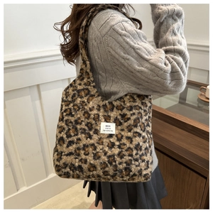Modische Plüsch-Tragetasche mit Leopardenmuster und weißem Markenlabel auf grauem Strickpullover