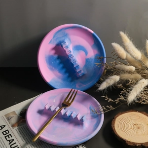 Détail d'un plateau rond texture marbre avec support ondulé tenant une fourchette dorée
