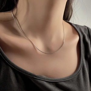 Close-up of a minimalist silver stainless steel box chain necklace worn on the neck