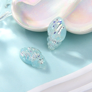 Macro shot of two light blue resin shell charms with shimmering iridescent foil flakes