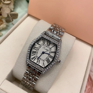 Close-up of a silver tonneau-shaped watch with rhinestone bezel and Roman numerals