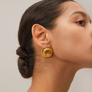 Close-up of 18k gold fish scale textured square stud earrings on model's ear