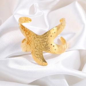 Macro detail of golden starfish-shaped adjustable cuff with hammered metal texture