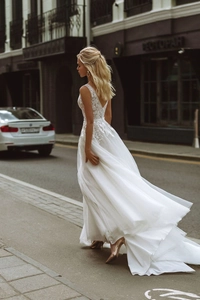 Detail view of floral lace bodice and long tulle train of a white deep V-neck wedding gown