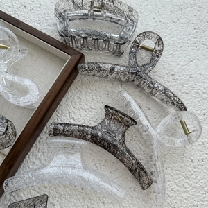 Close-up of transparent lace mesh hair claws with gold springs on a textured background
