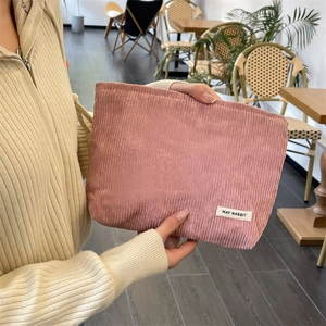 Pink corduroy makeup bag with 'MAY RABBIT' label held by hand in a cozy cafe setting