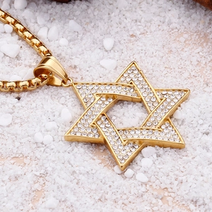 Close-up of gold hexagram pendant necklace with clear crystals on white pebbles
