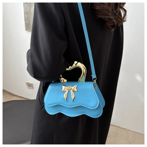 Detail of blue wavy textured leather bag with gold bow heart and liquid metal handle