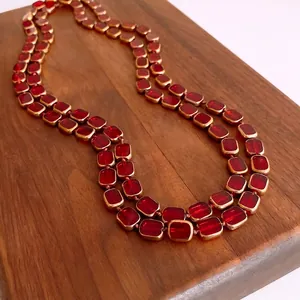 Double-layered gold necklace with oval red glass beads on a vintage wooden background