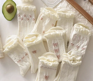 Close-up of white lace socks featuring pink flower embroidery and ruffle cuffs