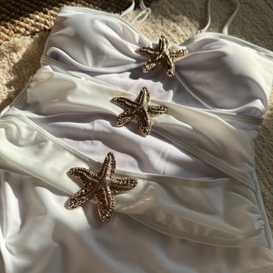 Detailed close-up of three golden starfish buckles on white swimwear fabric