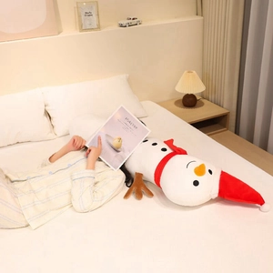 Long snowman plush pillow with red scarf and hat on a cozy bed in a warm bedroom
