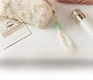Detail of plush cream makeup bag featuring fluffy texture and woven colorful zipper pull