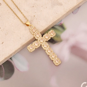 Macro shot of gold cross necklace with clear zircons on a textured stone surface