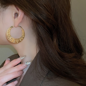 Detailed close-up of chunky golden twisted hoop earring with radiant pleated texture