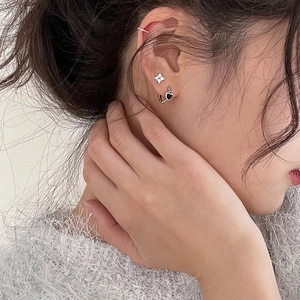 Chic silver clover stud and black heart drop earrings worn by a model in a close-up