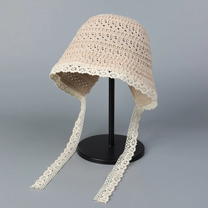 Detail of beige crochet sun hat with delicate white lace trim and long ribbon straps