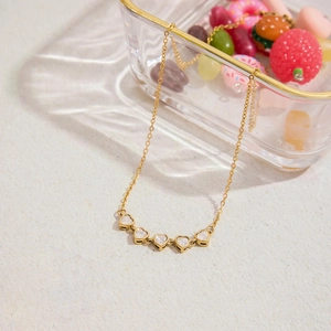 Detail of a gold stainless steel necklace featuring five zircon-inlaid heart pendants