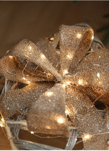 Macro detail of burlap Christmas bow with warm yellow LED lights and rustic texture