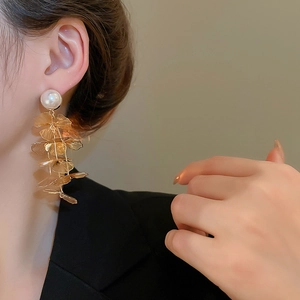 Close-up of golden floral tassel earrings with pearls on a model showing drape and texture