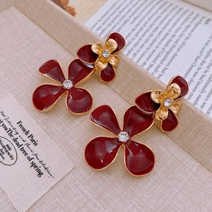 Macro detail of red oil-drop flower earrings with gold edges and crystal rhinestones