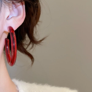 Close-up of a model wearing large translucent deep red resin C-shaped hoop earrings