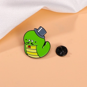 Cartoon green gentleman snake enamel pin with top hat on soft peach background
