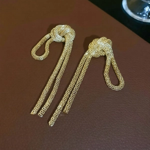 Detail of gold knot fringe earrings featuring delicate metallic woven mesh texture