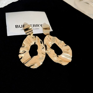 Macro detail of large wavy gold liquid metal earrings with polished texture on black velvet