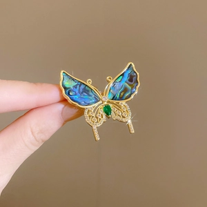 Détail macro d'une broche papillon plaquée or avec nacre bleue et pierre verte