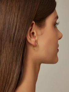 Close-up of a model wearing minimalist 14K gold-plated beaded hoop earrings in a warm light