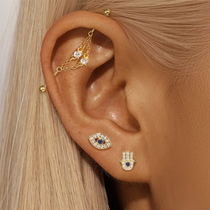 Macro shot of gold-plated industrial barbell ear set with evil eye and hamsa hand studs