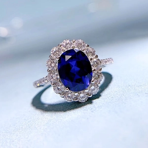 Macro shot of oval blue sapphire ring featuring classic diamond halo and pavé band details