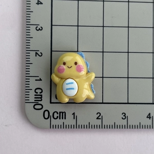 Macro shot of a small yellow resin dinosaur charm with ruler for size measurement