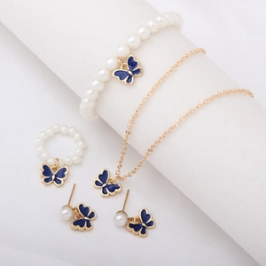 Parure bijoux dorée élégante avec papillons en émail bleu et perles blanches sur texture